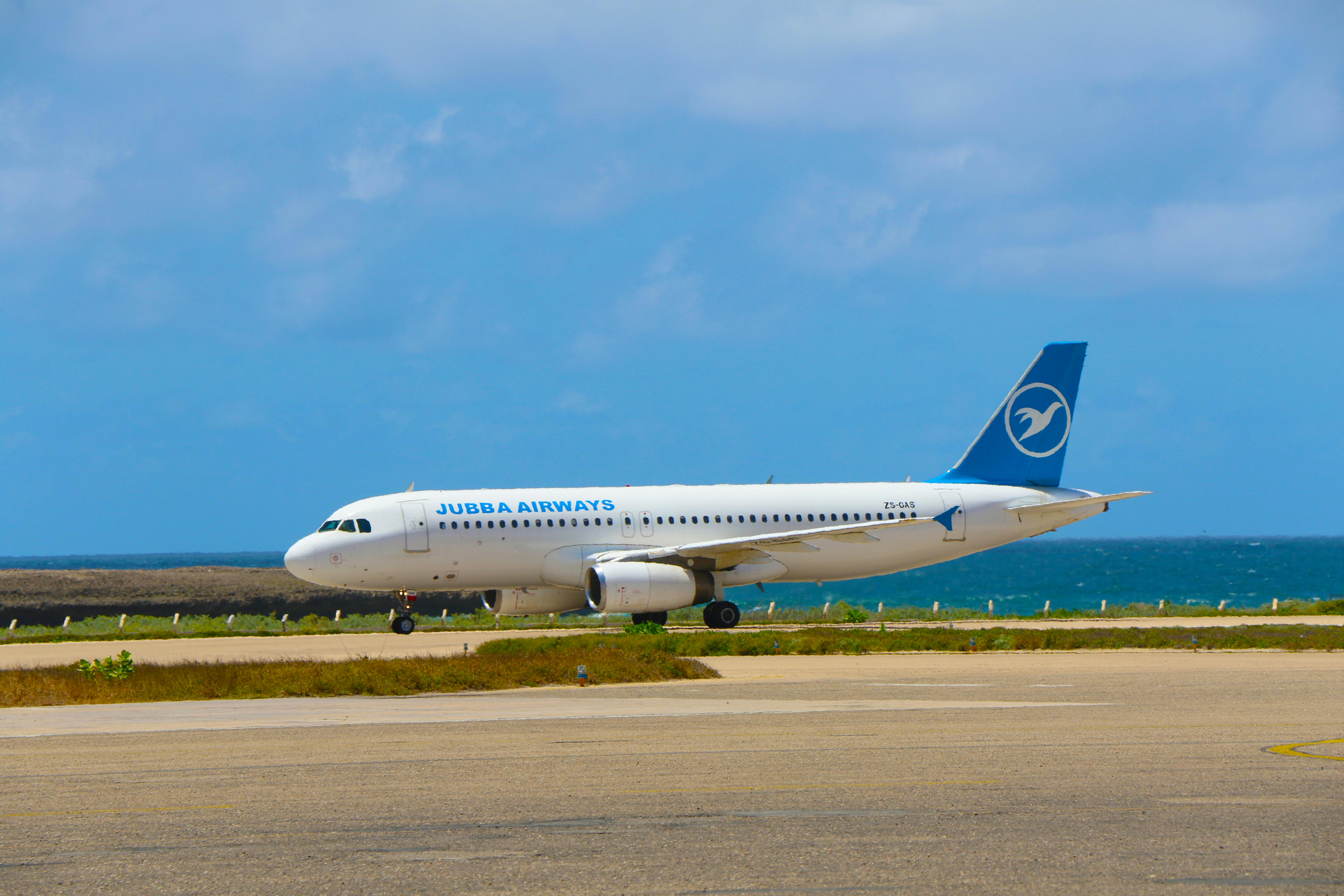 Jubba Airways airplane on runway near a body of water under a partly cloudy sky.